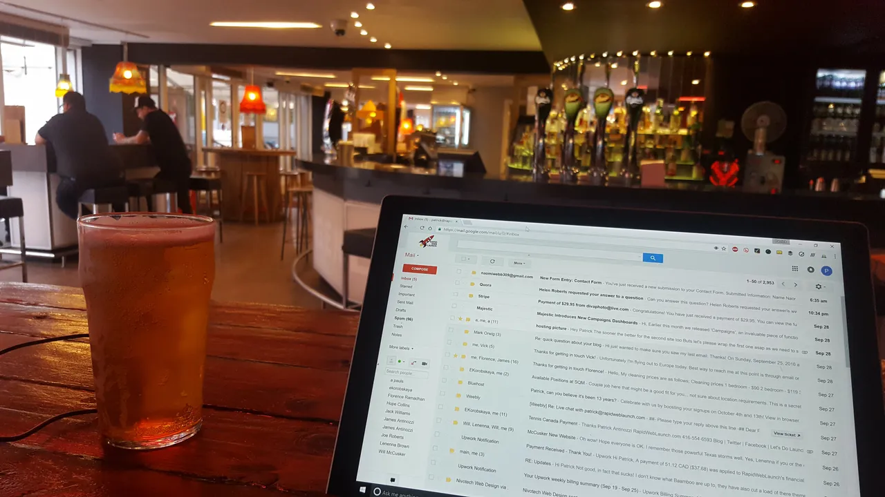 Patrick's laptop on a wooden bar table next to a glass of beer, with the pub's taps in the background.