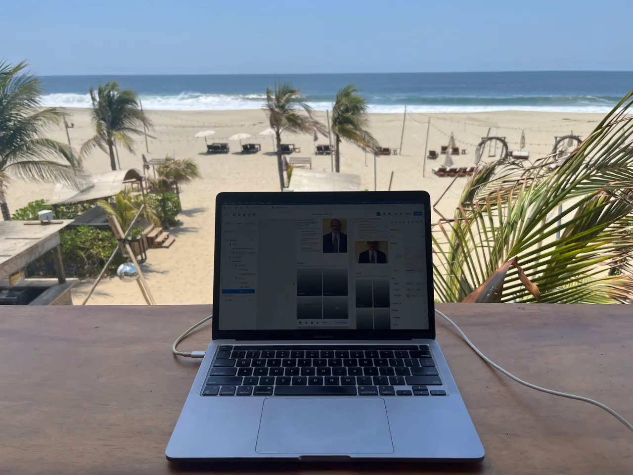 Patrick's laptop on a wooden desk overlooking a beach with palm trees.